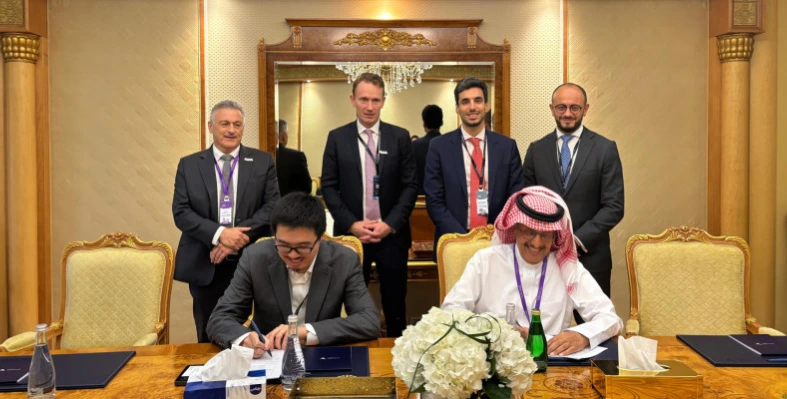 Two executives sign a joint development agreement at a formal table. 